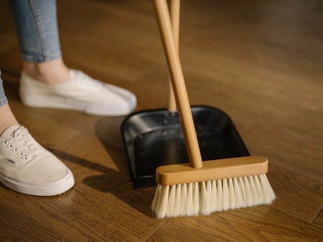 person in blue jeans and white should using a broom and dust pan